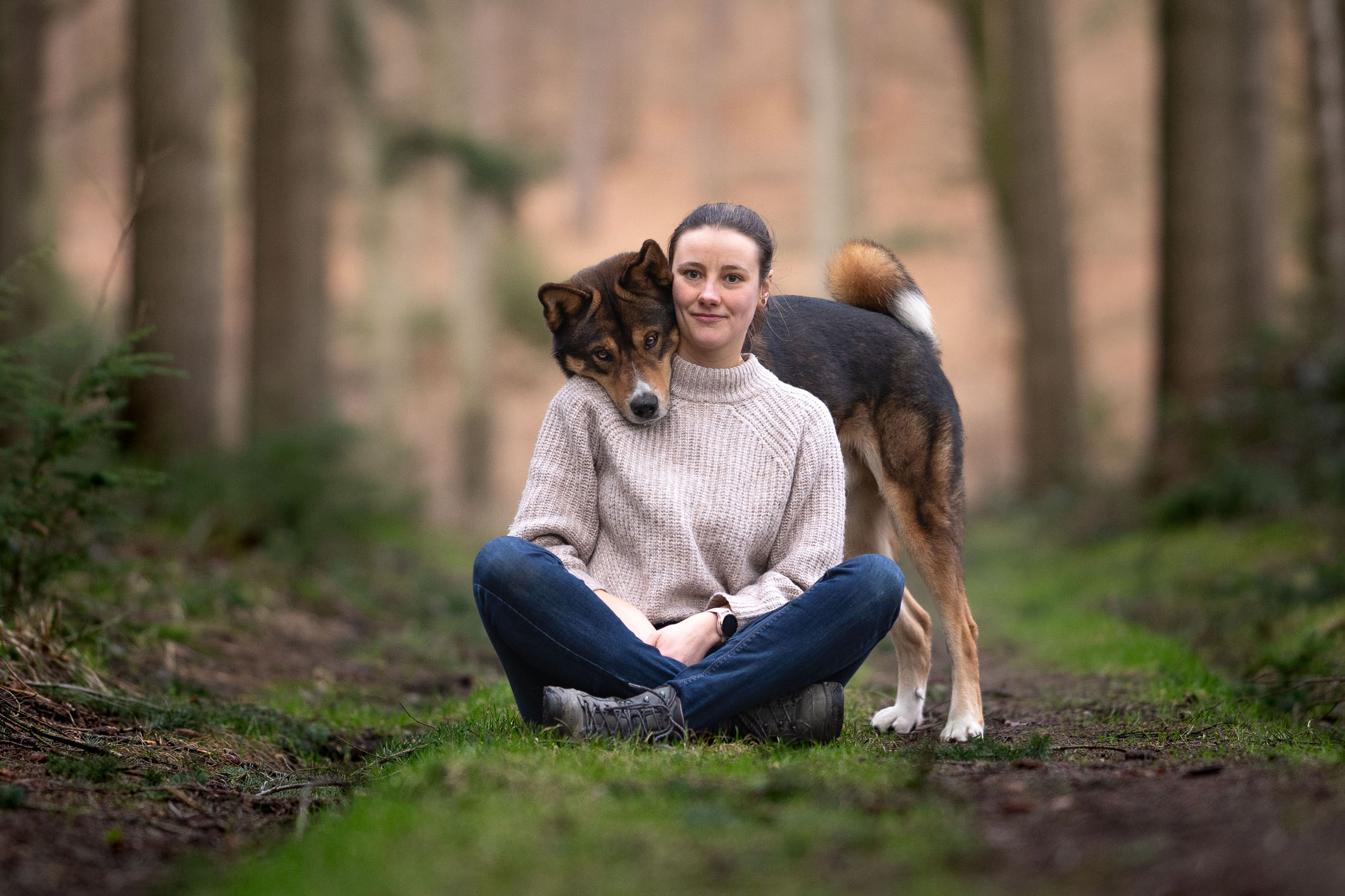 Hundetrainerin sitzt im Wald, Akita-Mix schaut über die Schulter Selfi-Trick Hundetraining Bielefeld